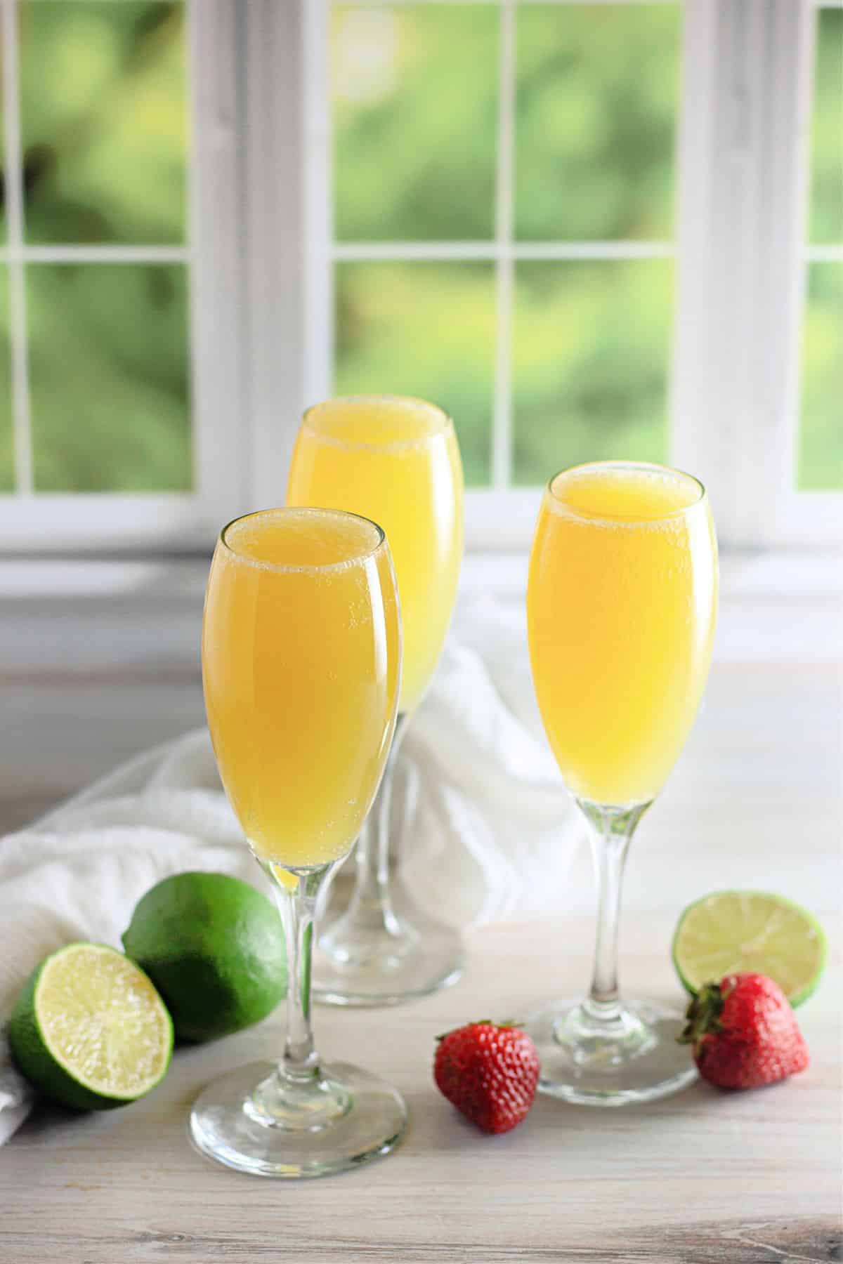 Three champagne glasses with virgin mimosas in front of a window.