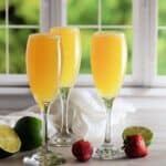 3 champagne glasses with mocktail mimosas in front of a window.