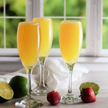3 champagne glasses with mocktail mimosas in front of a window.