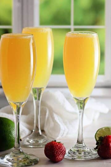 3 champagne glasses with mocktail mimosas in front of a window.