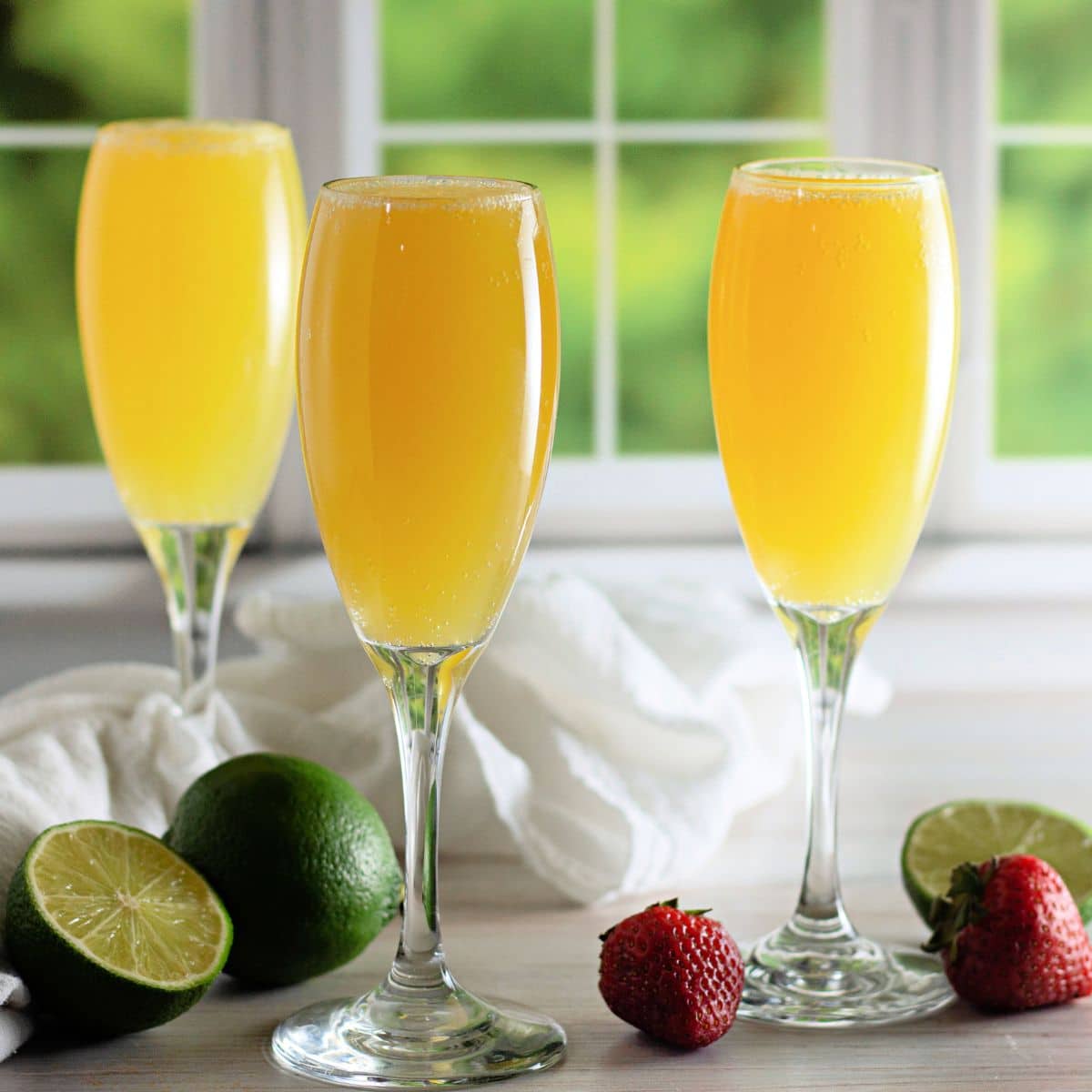 3 champagne glasses with mocktail mimosas in front of a window.