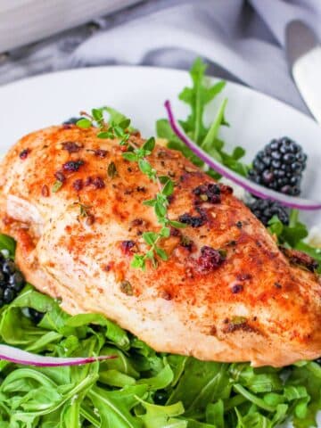 A baked chicken breast with blackberry glaze on a bed of lettuce.