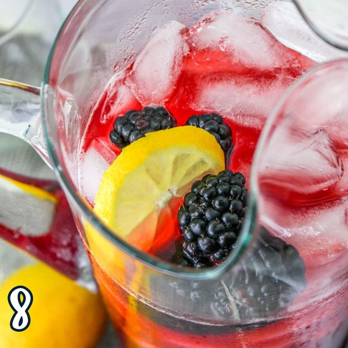 A pitcher of fresh blackberry lemonade filled with sliced lemons, blackberries, and ice. 