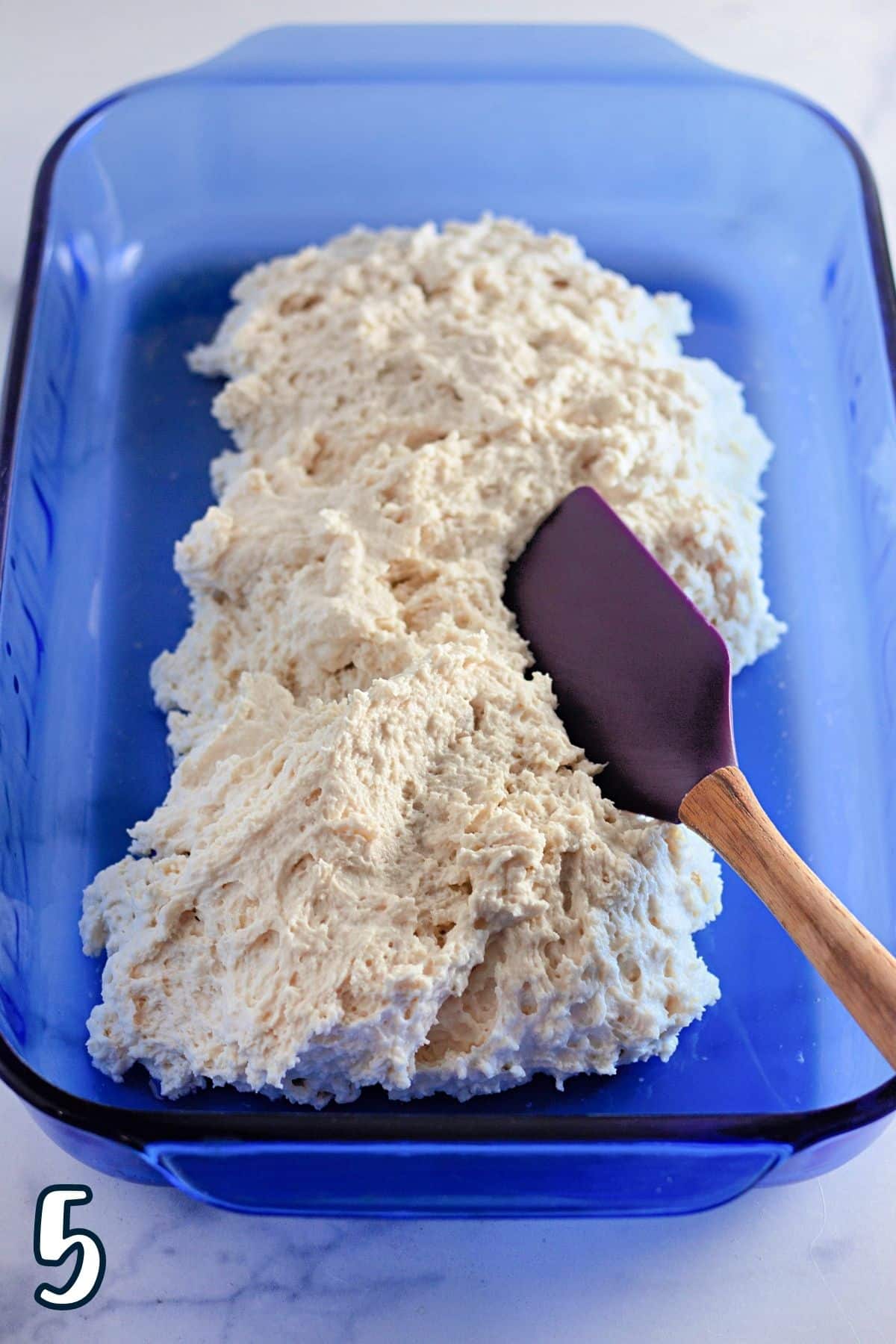 Biscuit dough being poured into a blue baking dish. 