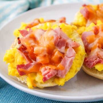 A plate full of mini bagels topped with eggs, ham and cheese.