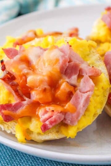 A plate full of mini bagels topped with eggs, ham and cheese.