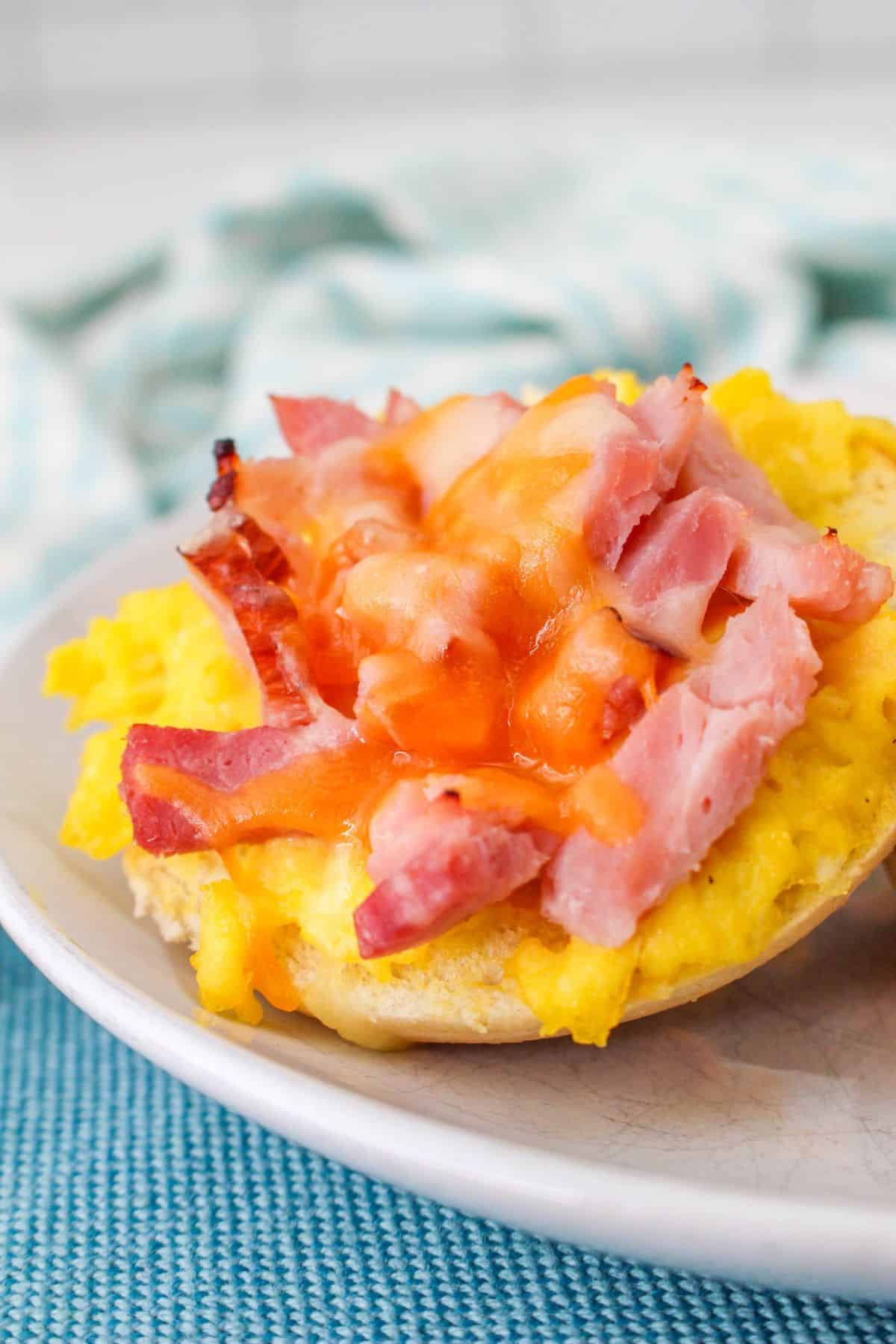 A plate full of mini bagels topped with eggs, ham and cheese.