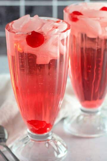 Two shirley temple drinks in clear glasses with ice.