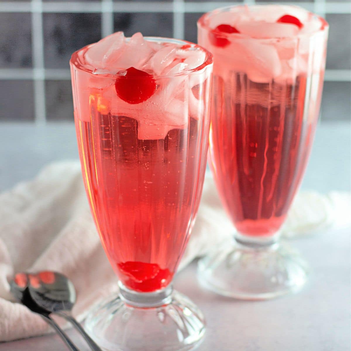 Two shirley temple drinks in clear glasses with ice.