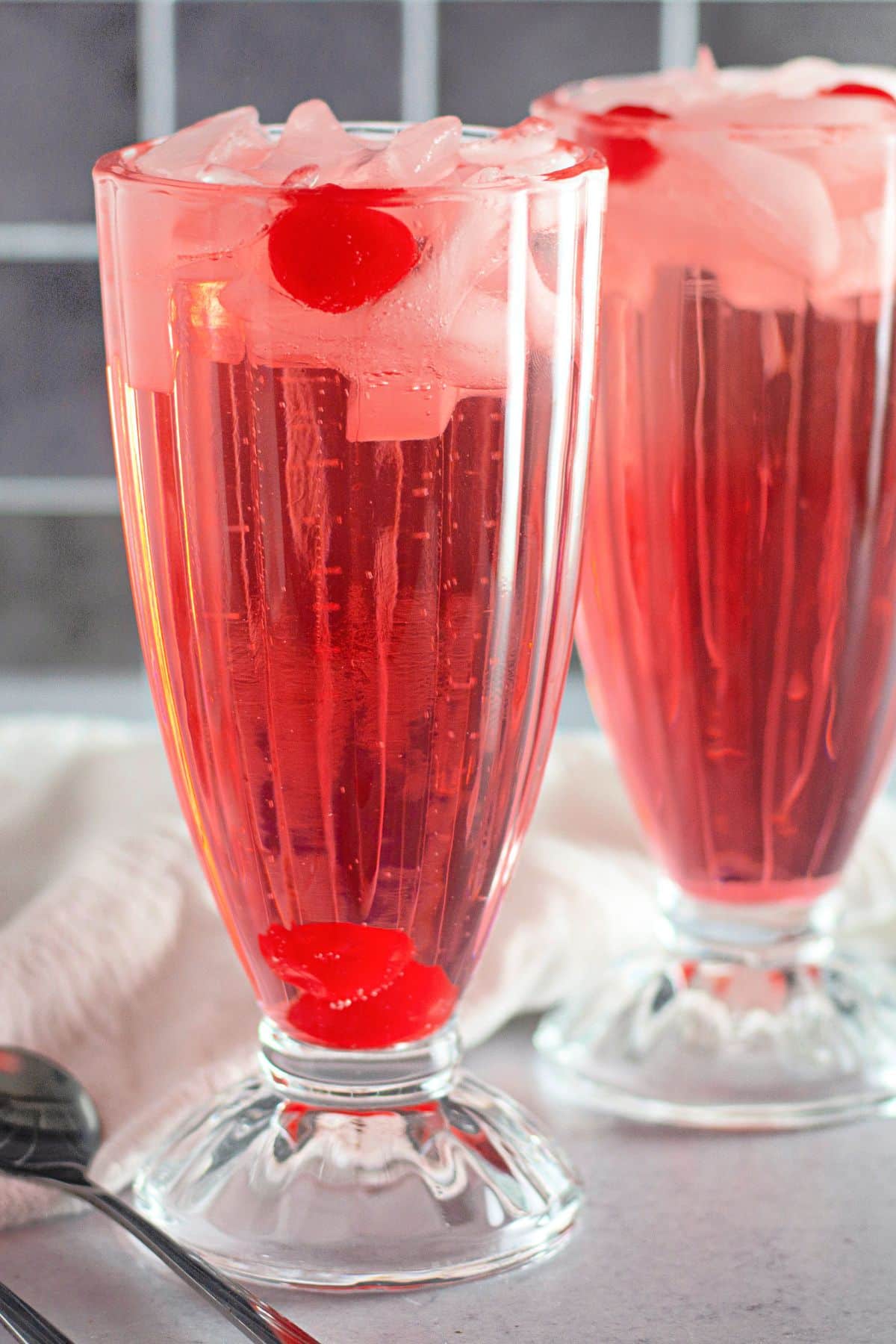 Two shirley temple drinks in clear glasses with ice.