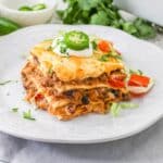 An individual serving of taco lasagna on a white plate next to a fork and taco toppings.