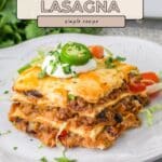 A slice of taco lasagna, a delicious taco casserole, topped with sour cream, cheese, and jalapeño on a white plate.