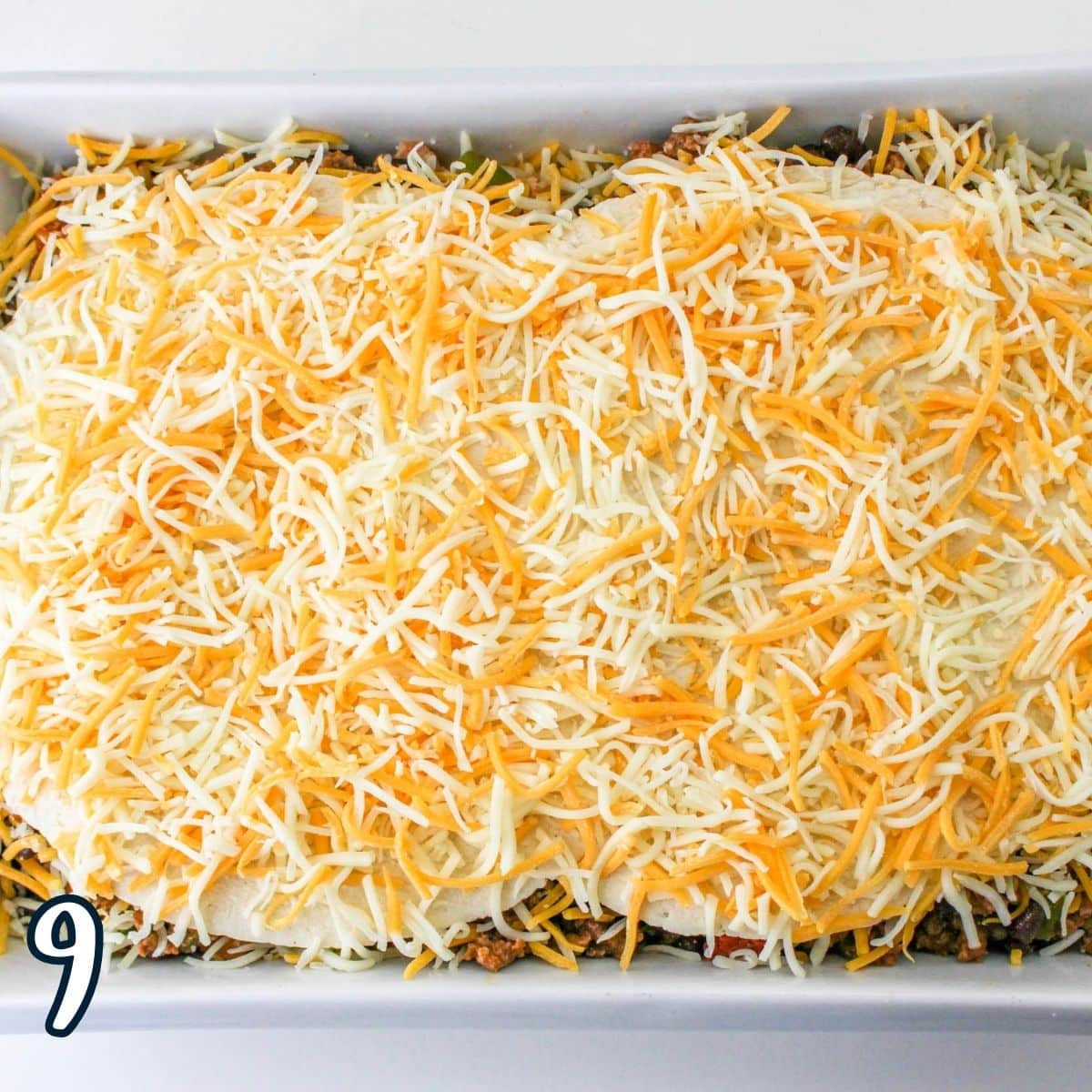 Cheese covered tortillas as the top layer of taco casserole in a baking dish. 