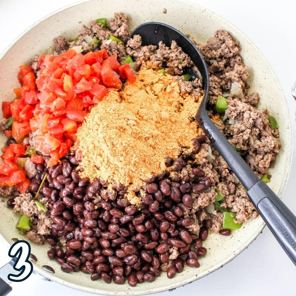 Beans and diced tomatoes added to cooked ground meat in a skillet. 