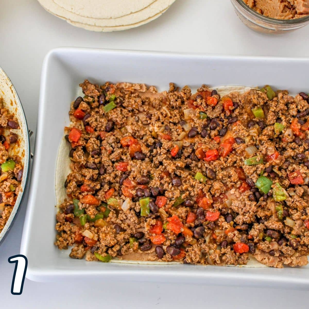Taco meat spread over tortillas in a baking dish. 