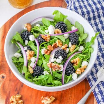 Arugula with blackberries and goat cheese in a white bowl.