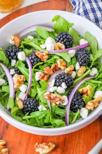 Arugula with blackberries and goat cheese in a white bowl.