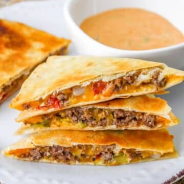Cheeseburger quesadillas stacked on a white plate next to a bowl of special sauce.