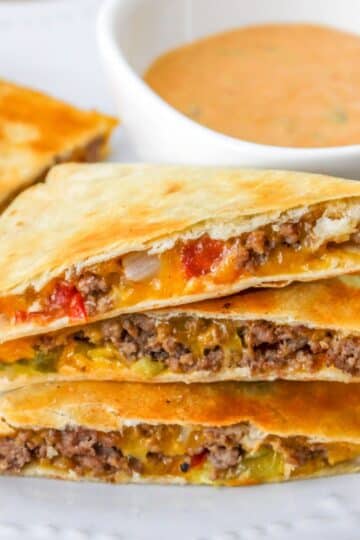 Cheeseburger quesadillas stacked on a white plate next to a bowl of special sauce.