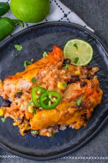 Baked chicken strips with beans and rice on a black plate.