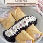 Four folded Blueberry Crepes filled with pink cream, topped with blueberry sauce and whipped cream on a white plate.