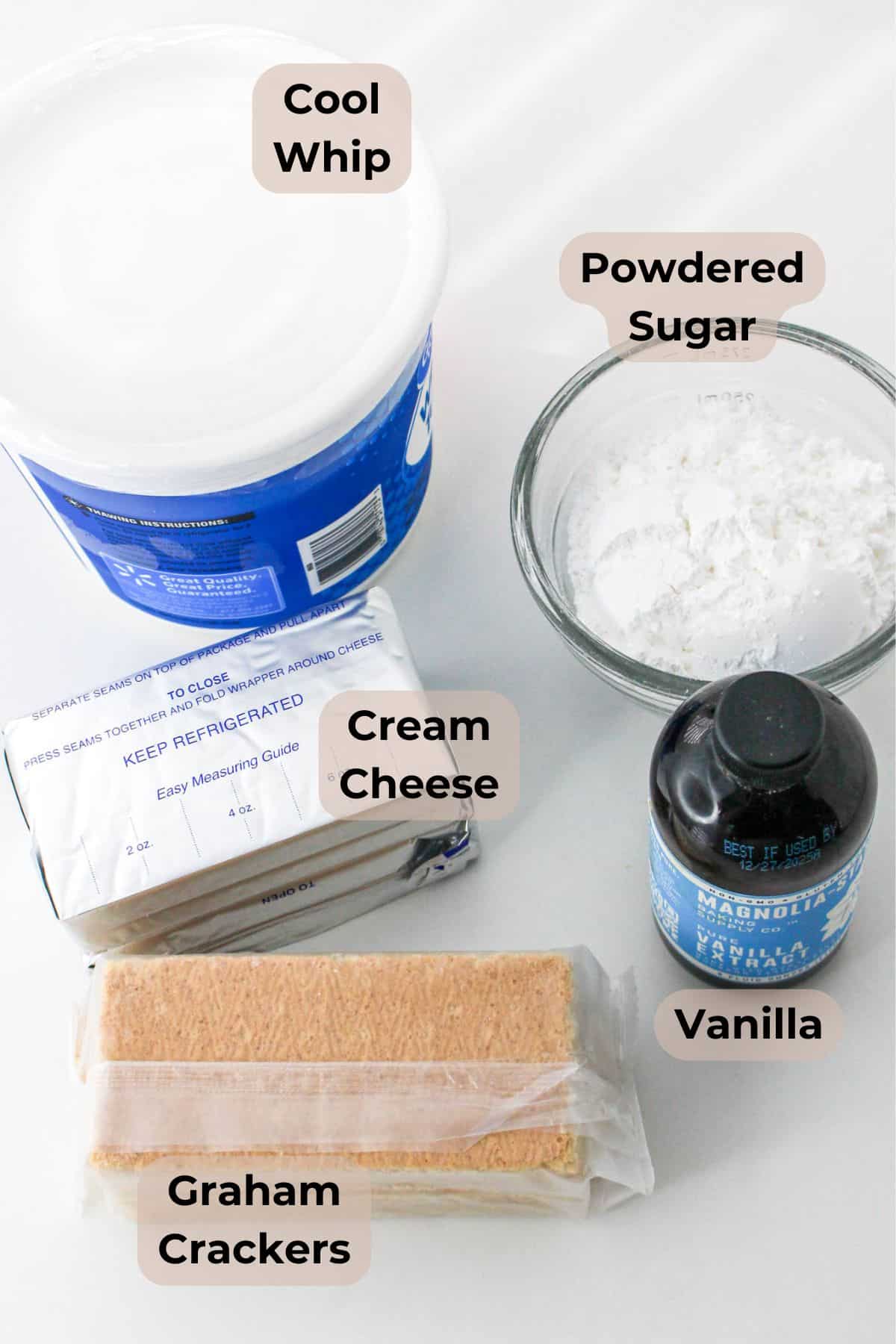 Labeled ingredients: Cool Whip, powdered sugar, cream cheese, vanilla, and graham crackers on a white surface.