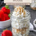A mason jar filled with rich Cheesecake Mousse, topped with whipped cream and crumbs, with fresh strawberries nearby.