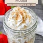 Mason jar filled with creamy cheesecake mousse, topped with crumbs, next to strawberries on a table.