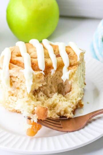 A cinnamon rolls with apples on a white plate next to green apples.