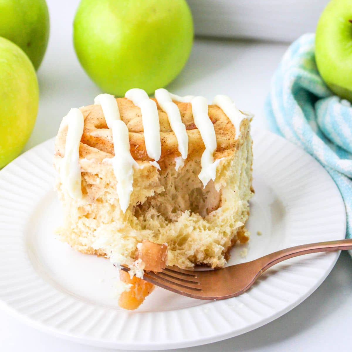 A cinnamon rolls with apples on a white plate next to green apples.