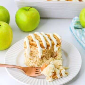 A cinnamon rolls with apples on a white plate next to green apples.