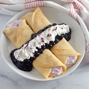 Two crepes filled with cream cheese and topped with blueberry sauce and whipped cream.