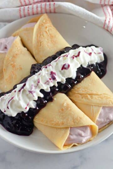 Two crepes filled with cream cheese and topped with blueberry sauce and whipped cream.