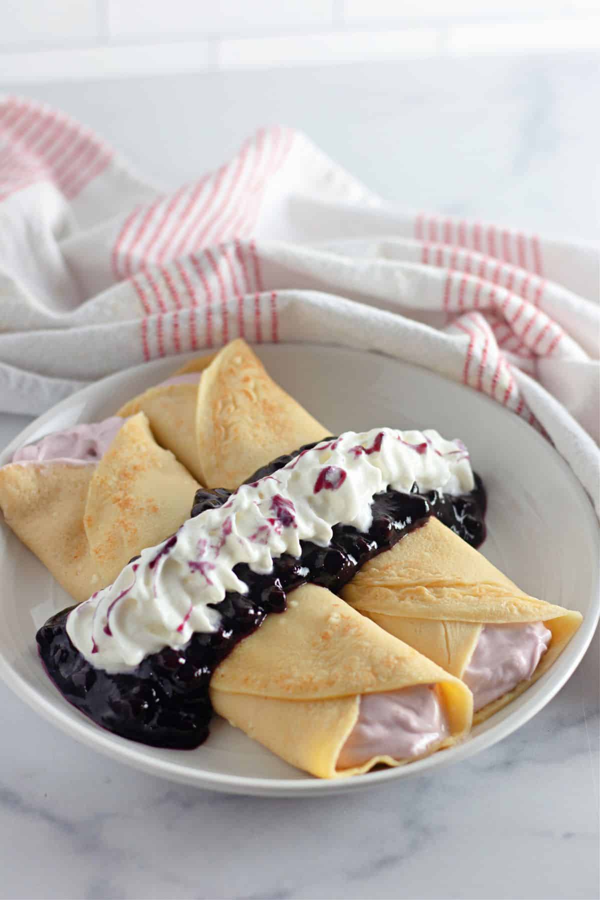Two crepes filled with cream cheese and topped with blueberry sauce and whipped cream. 