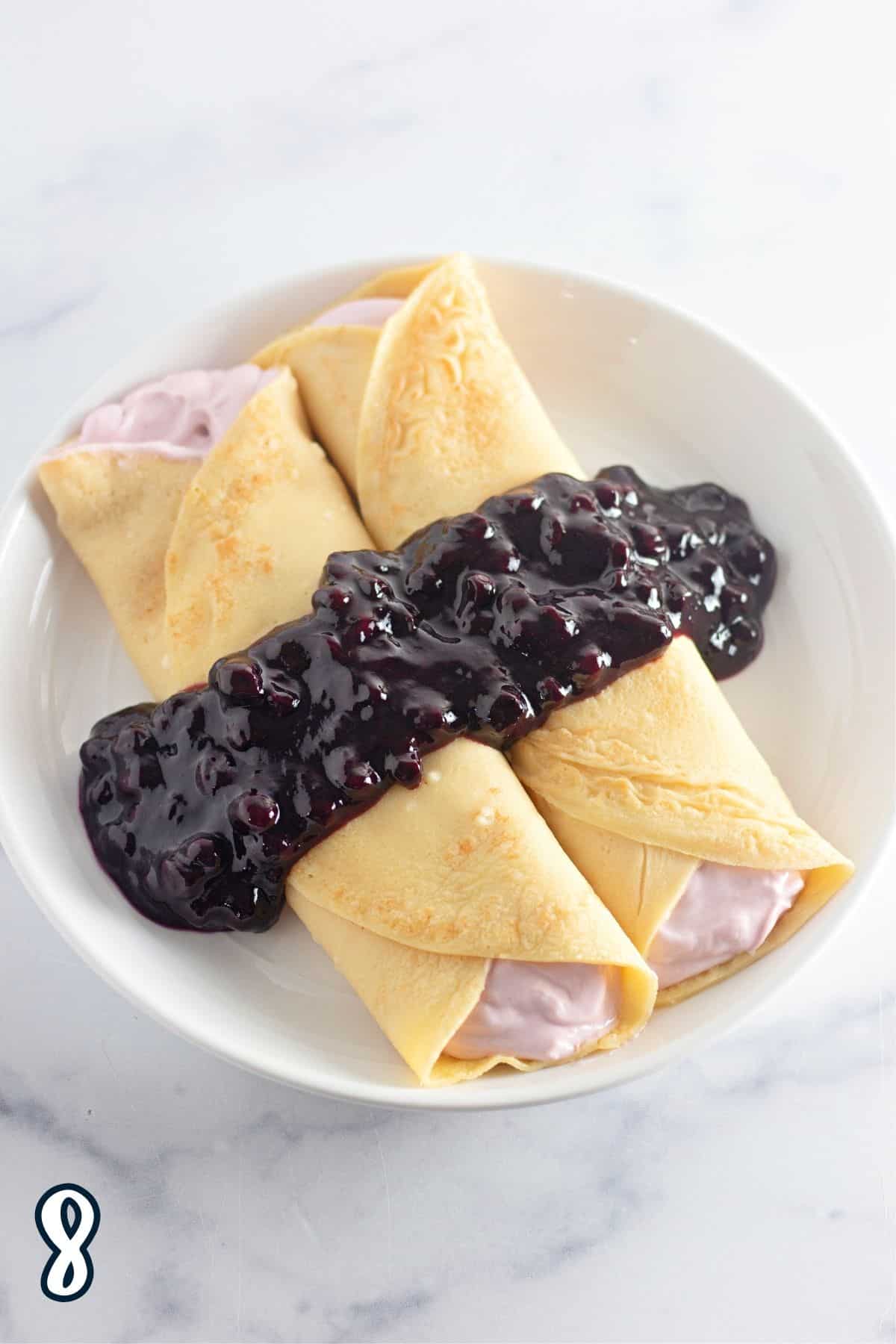Blueberry sauce poured over crepes on a white plate. 