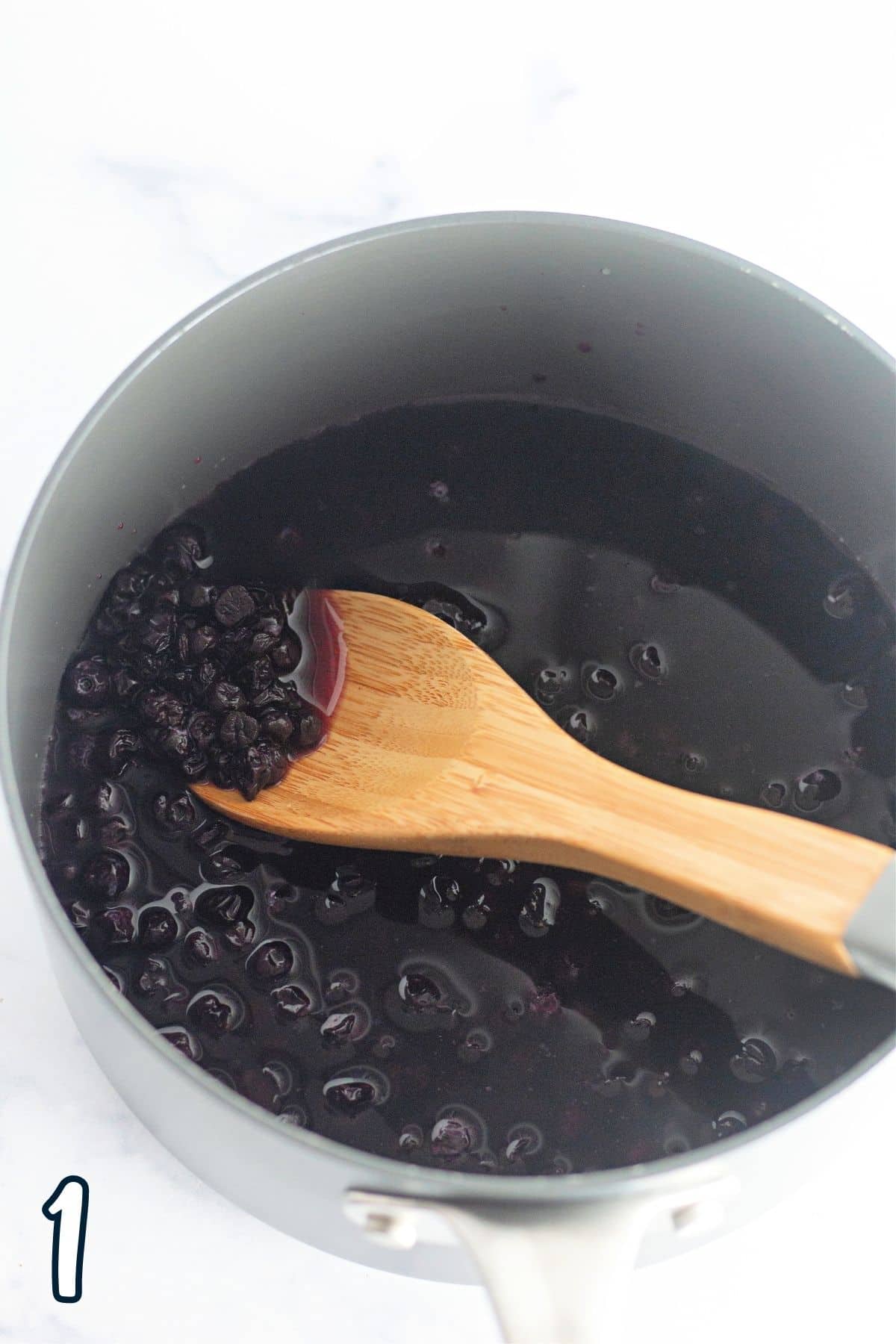 Blueberry sauce in a saucepan with a wooden spoon. 