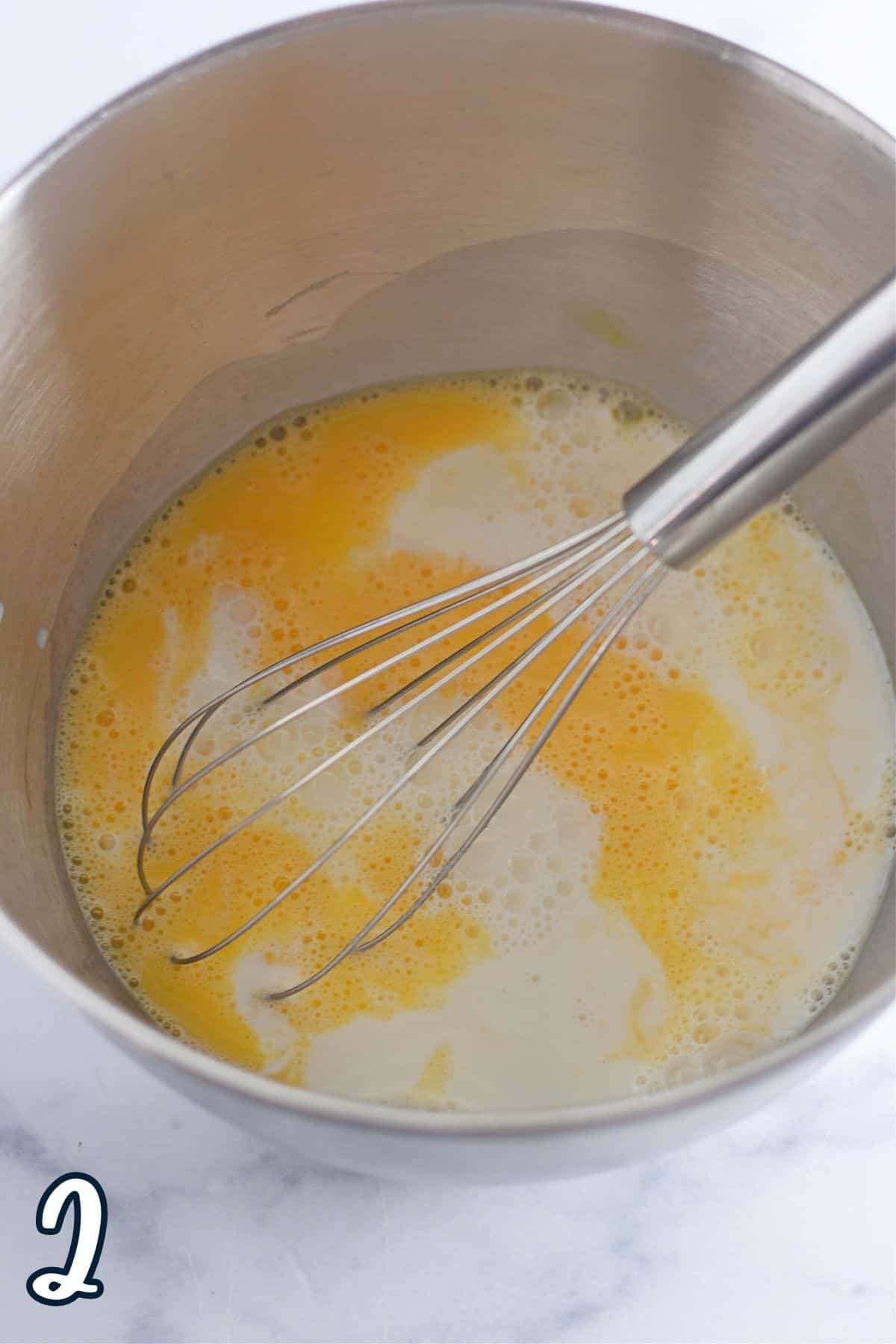 Eggs and milk with a whisk in a metal mixing bowl. 