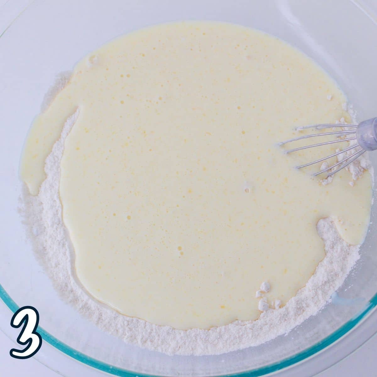 Buttermilk mixed with eggs and butter added to a flour mixture in a glass bowl. 