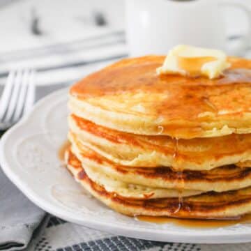 A stack of pancakes topped with butter and syrup on a white plate.