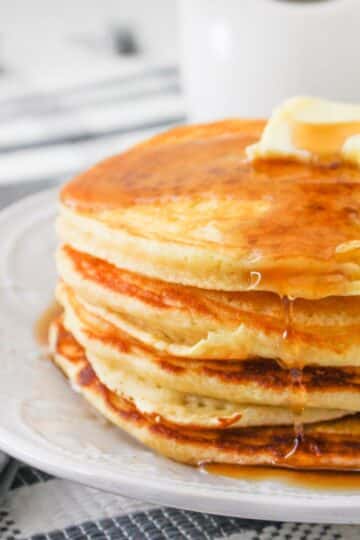 A stack of pancakes topped with butter and syrup on a white plate.