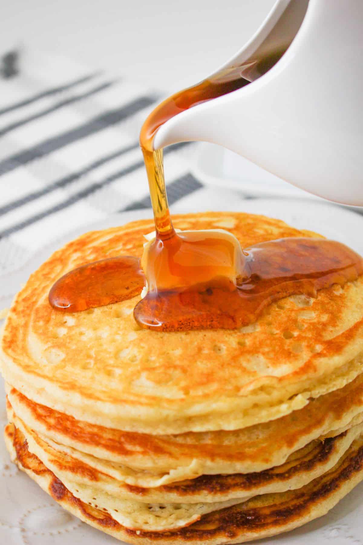 Syrup being poured over a stack of pancakes. 