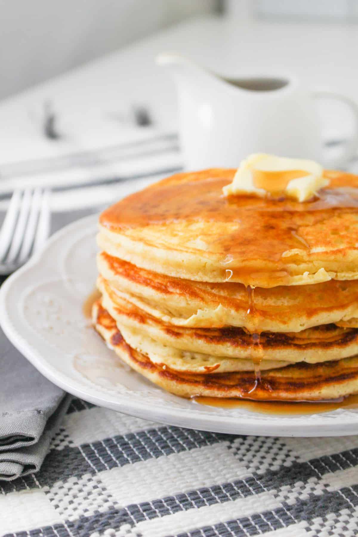 A stack of pancakes topped with butter and syrup on a white plate. 
