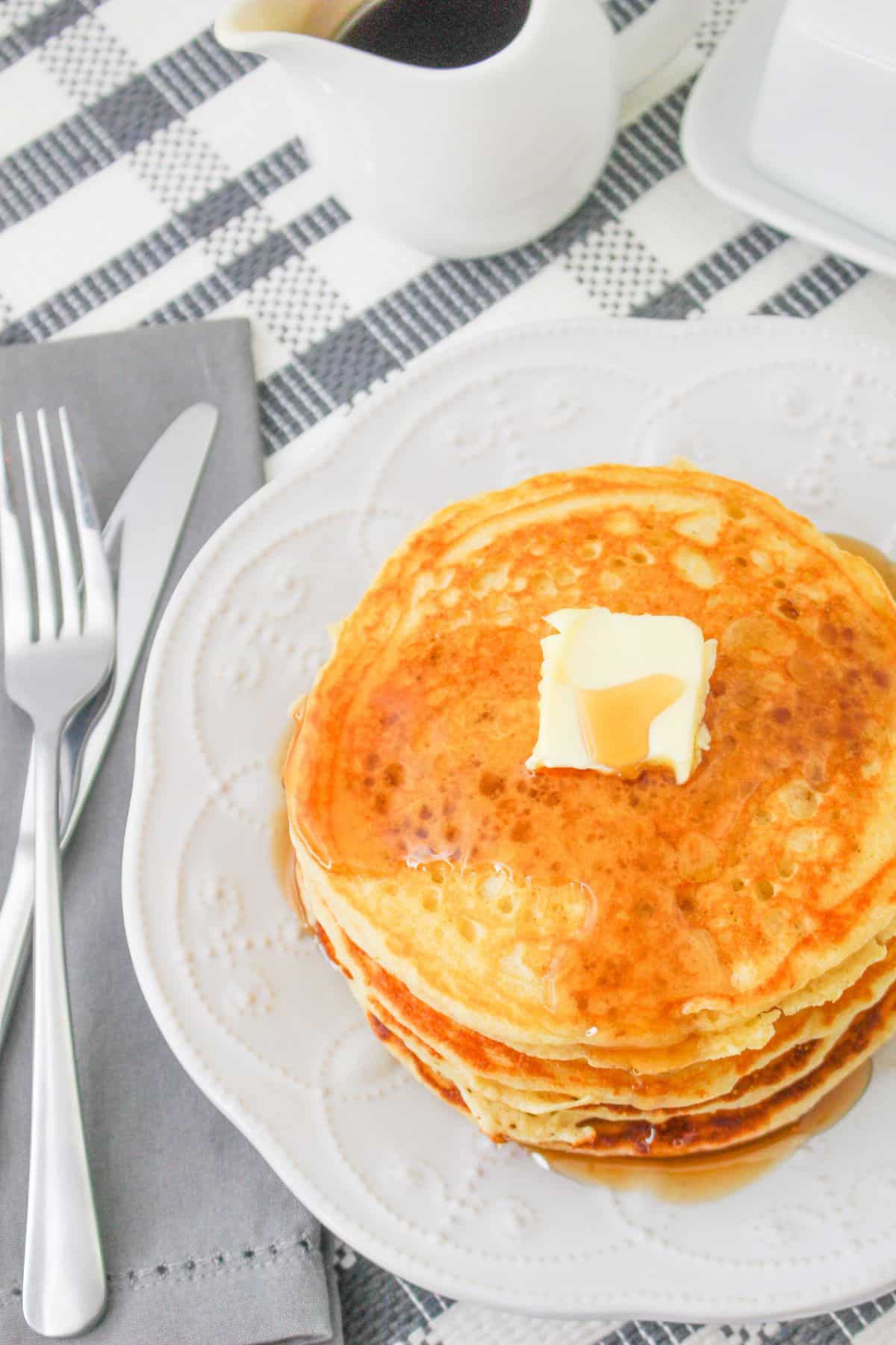 A stack of pancakes topped with a pat of butter and syrup on a white plate. 