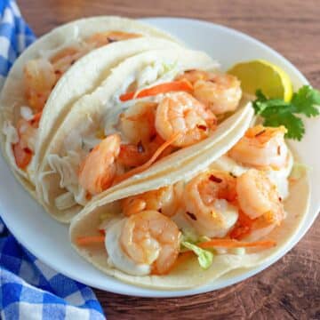 Corn tortillas filled with slaw and shrimp on a plate.