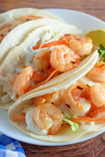 Corn tortillas filled with slaw and shrimp on a plate.
