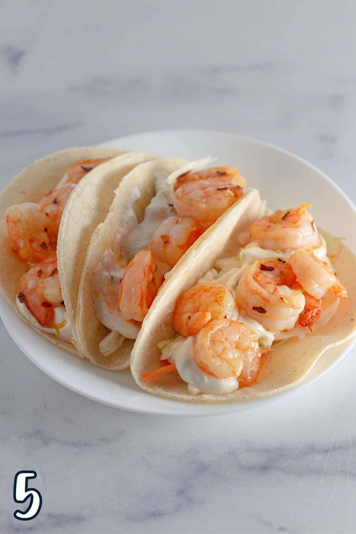Cooked shrimp laid over a bed of shredded cabbage and cilantro sauce in a taco shell.