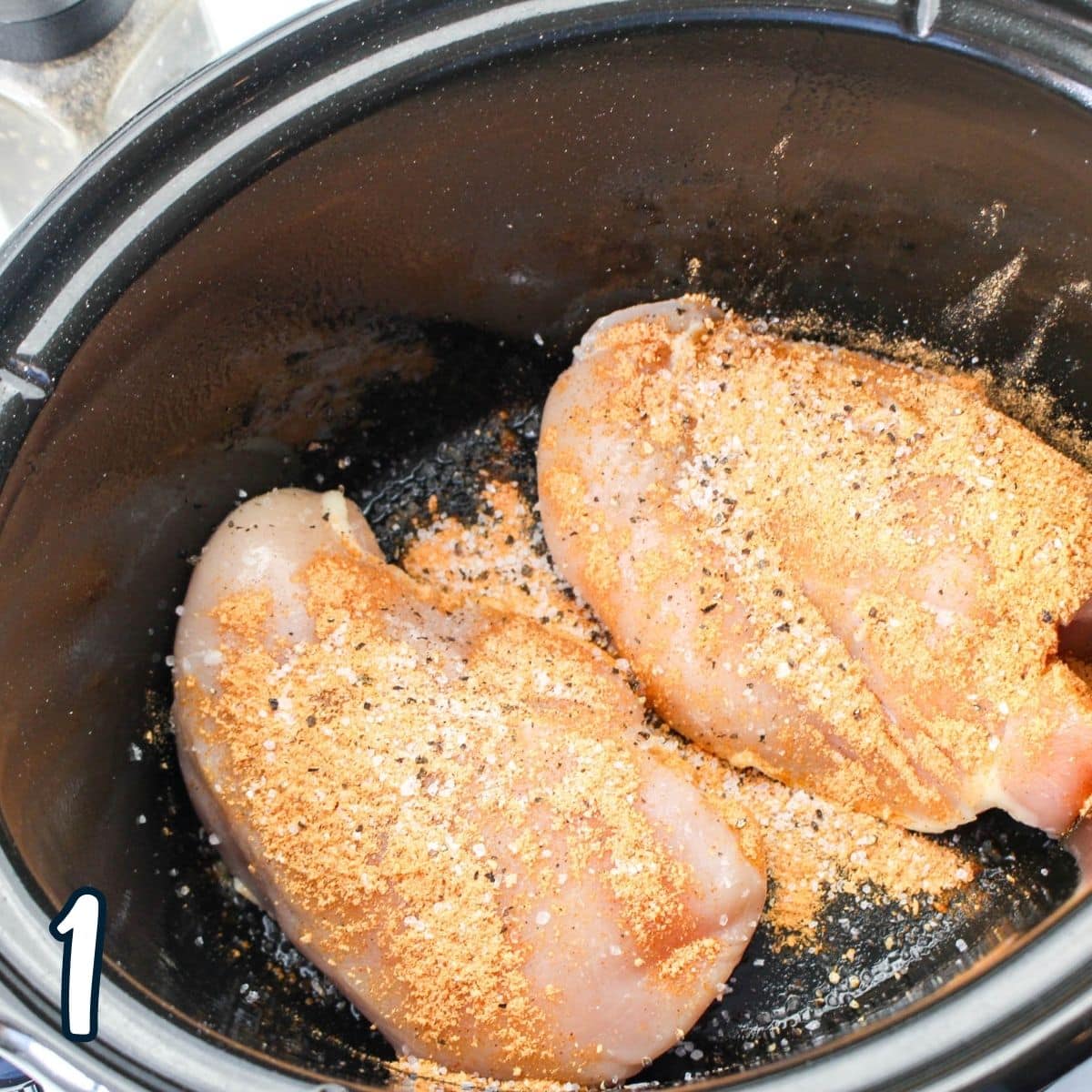 Seasoned chicken breasts in a slow cooker bowl. 