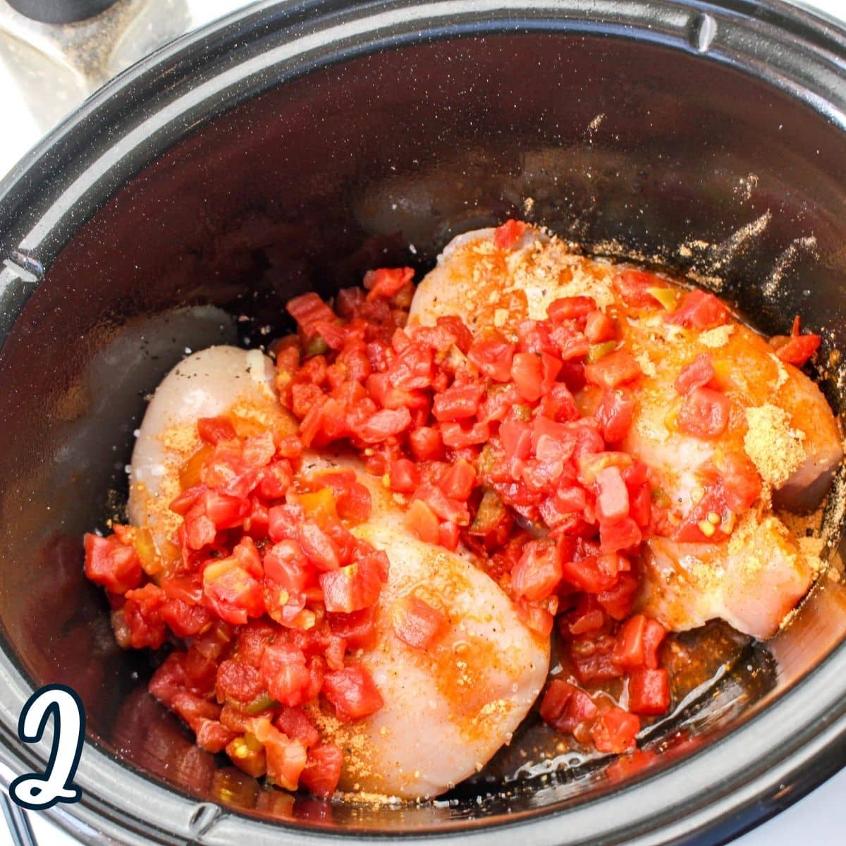 Diced tomatoes over chicken in a slow cooker. 