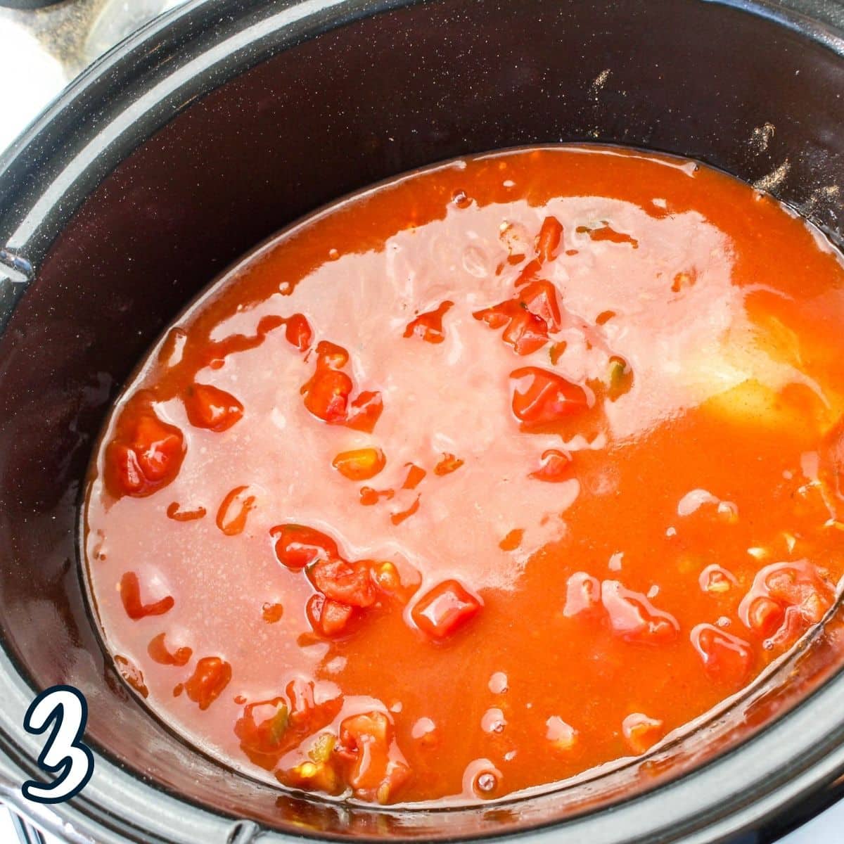 Enchilada sauce poured over chicken in a slow cooker. 