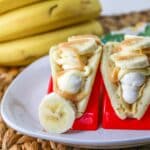 Pancakes filled with cheesecake mousse, bananas, and topped with caramel on a white plate.